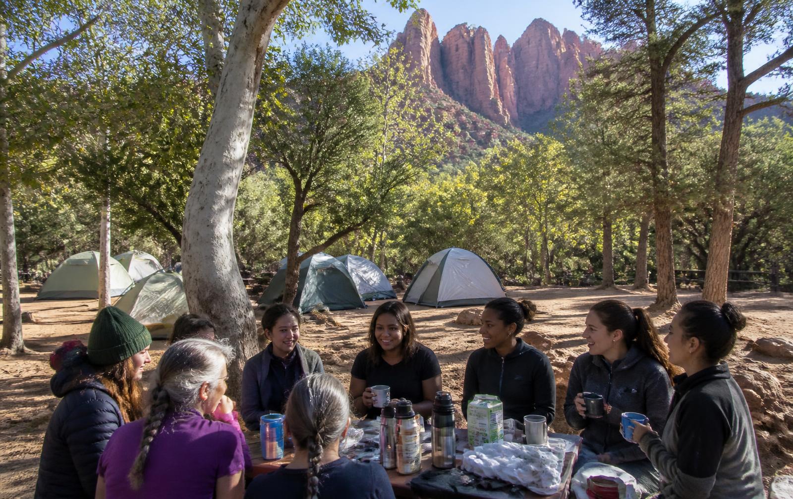 Small group of adults talking over coffee at a forest campground